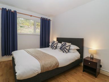 A bedroom with a double bed with two crab patterned cushions a bedside table with a lamp and a window with dark curtains at 26 Manorcombe in St Ann's Chapel Cornwall