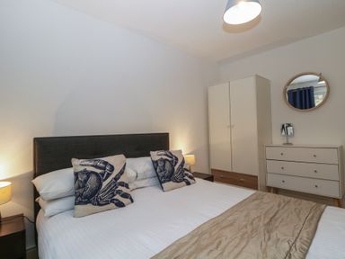 A bedroom with a bed with crab pillows a wardrobe a chest of drawers and a round mirror at 26 Manorcombe in St Ann's Chapel Cornwall