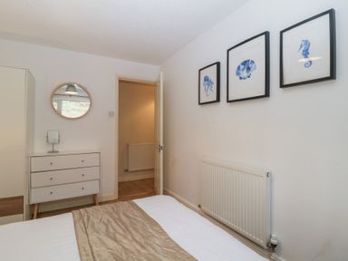 A bedroom with a bed a dresser with a small mirror a round wall mirror three framed sea creature pictures and a radiator at 26 Manorcombe St Ann's Chapel Cornwall