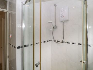 A shower enclosure with a glass door electric shower and tiled walls at 26 Manorcombe in St Anns Chapel Cornwall