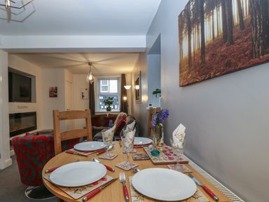 A dining table set for four adjacent to a living room with chairs sofa and wall art at Colliers Cottage in Cinderford