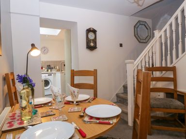 A dining area with a round wooden table set for four next to a staircase and kitchen at Colliers Cottage in Cinderford