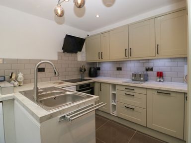 A kitchen with a sink a stove toaster and beige cabinets at Colliers Cottage in Cinderford