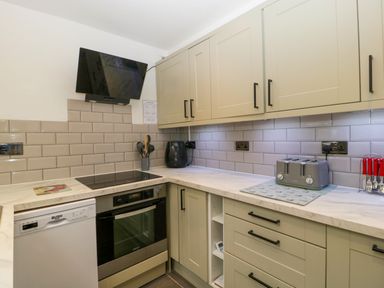 A kitchen with beige cabinets a dishwasher an oven a stovetop a black extractor fan a toaster and utensils at Colliers Cottage in Cinderford