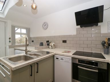 A kitchen with a sink, stove, oven, dishwasher, clock on the wall, and utensils in a container at Colliers Cottage in Cinderford