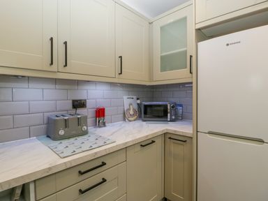 A kitchen corner with white cabinets a refrigerator a toaster a microwave and a knife set at Colliers Cottage in Cinderford