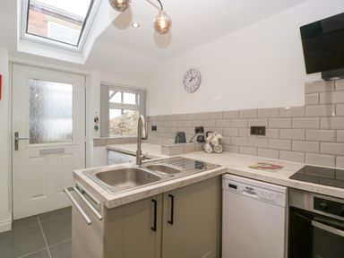 A kitchen with a sink, dishwasher, oven, and a door with a window at Colliers Cottage in Cinderford
