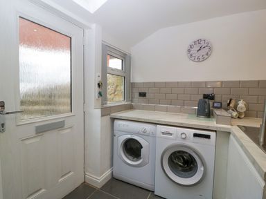 A laundry room with a washing machine and dryer under a countertop next to a door and window at Colliers Cottage in Cinderford
