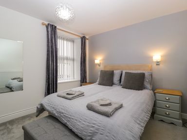 A bedroom with a double bed bedside tables a window with curtains and wall lights at Colliers Cottage in Cinderford