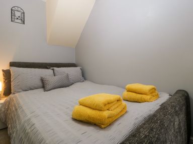 A bedroom with a gray bedspread and two sets of yellow towels on the bed at Colliers Cottage in Cinderford