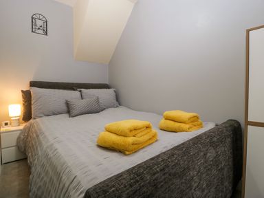A bedroom with a double bed gray bedding yellow towels on the bed a bedside table with a lamp and a white wardrobe at Colliers Cottage in Cinderford