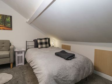 A bedroom with a bed covered in gray bedding and pillows near a small side table and a gray armchair at Colliers Cottage in Cinderford