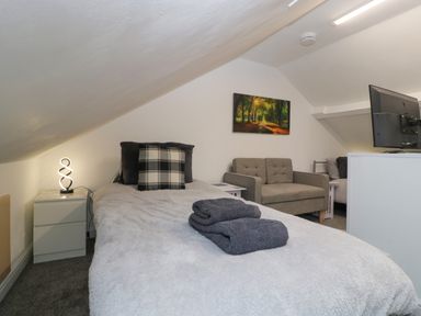 A bedroom with a single bed towels on the bed a small sofa a nightstand with a lamp and a television in Colliers Cottage in Cinderford