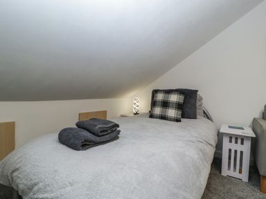 A single bed with gray bedding a plaid pillow and folded towels under a sloped ceiling at Colliers Cottage in Cinderford