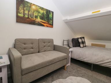 A small room with a gray sofa a bed with pillows a side table and a landscape picture on the wall at Colliers Cottage in Cinderford
