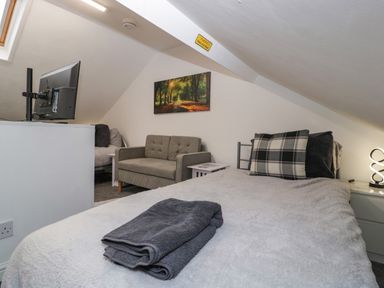 A bedroom with a bed with folded towels a small sofa a TV on a stand and a picture on the wall at Colliers Cottage in Cinderford