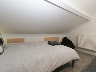A bedroom with a bed covered with a gray blanket a black bean bag chair and a radiator on the wall at Colliers Cottage in Cinderford