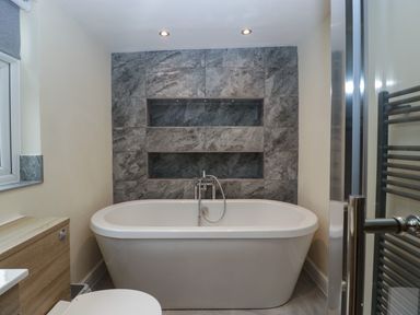 A bathroom with a freestanding bathtub and tiled wall shelves at Colliers Cottage in Cinderford