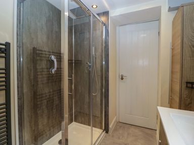 A bathroom with a glass shower enclosure a white door and wooden cabinets at Colliers Cottage in Cinderford