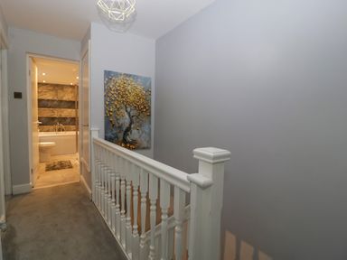 A hallway with a white banister a painting on the wall and a bathroom at Colliers Cottage in Cinderford