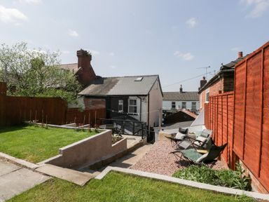 An outdoor garden area with green grass, a stone pathway, folding chairs on gravel, and red wooden fences at Colliers Cottage in Cinderford