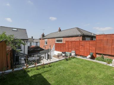 A backyard with a grass lawn a wooden fence outdoor seating and neighboring houses at Colliers Cottage in Cinderford