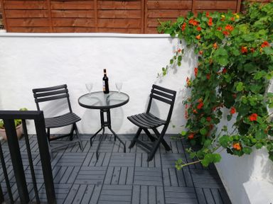 A patio with a table and chairs, wine bottle and glasses at Colliers Cottage in Cinderford