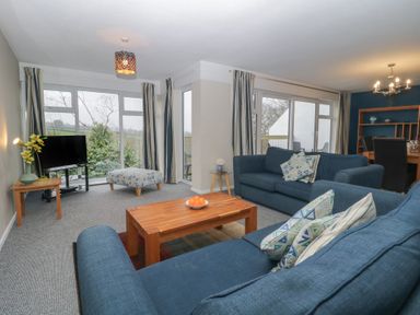A living room with blue sofas a wooden coffee table and a TV next to large windows at Tamar Cottages 34 St Ann's Chapel Cornwall