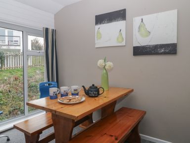 A wooden dining table with benches cups a teapot and a vase with flowers by a window at Tamar Cottages 34 in St Ann's Chapel Cornwall
