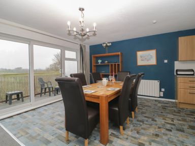 A dining area with a wooden table and six leather chairs next to sliding glass doors at Tamar Cottages 34 St Ann's Chapel Cornwall