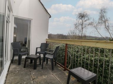 A balcony with black plastic chairs and tables overlooking greenery at Tamar Cottages 34 in St Ann's Chapel Cornwall