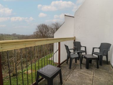 A balcony with four black chairs and two black tables overlooking trees and grass at Tamar Cottages 34 in St Ann's Chapel Cornwall