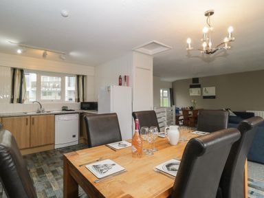 A dining table set with plates, glasses, and a bottle in a kitchen and living area at Tamar Cottages 34 in St Ann's Chapel, Cornwall