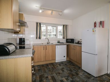 A kitchen with wooden cabinets a white dishwasher a white fridge and a window with curtains at Tamar Cottages 34 St Ann's Chapel Cornwall