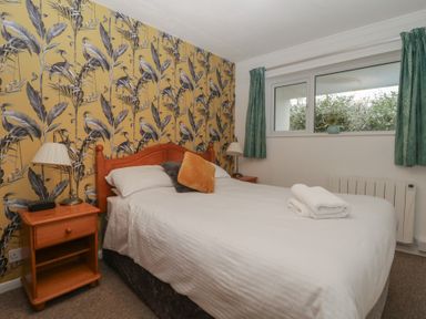 A bedroom with a double bed with white bedding two pillows a wooden headboard bedside tables with lamps and a window with green curtains at Tamar Cottages 34 in St Ann's Chapel Cornwall
