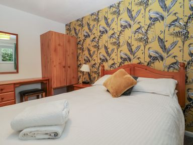 A bedroom with a double bed white towels on the bed a wooden wardrobe a desk with a mirror and patterned wallpaper at Tamar Cottages 34 in St Ann's Chapel Cornwall