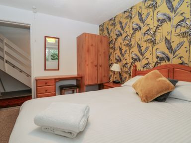 A bedroom with a bed a wooden wardrobe a desk with a stool and a mirror and patterned wallpaper at Tamar Cottages 34 St Ann's Chapel Cornwall