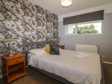 A bedroom with a double bed two bedside tables with lamps a window and patterned wallpaper at Tamar Cottages 34 St Ann's Chapel Cornwall