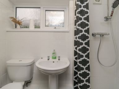 A bathroom with a toilet, sink, shower with a black and white curtain, and a window with frosted glass at Tamar Cottages 34 St Ann's Chapel Cornwall
