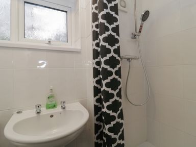 A bathroom with a sink and soap dispenser next to a shower with a patterned curtain at Tamar Cottages 34 in St Ann's Chapel Cornwall