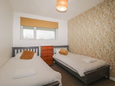 A bedroom with two single beds separated by a wooden chest of drawers and a window with a mustard blind at Tamar Cottages 34 St Ann's Chapel Cornwall