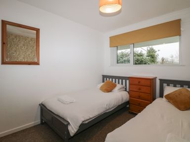 A bedroom with two single beds, a wooden chest of drawers, a window with a yellow blind, a wooden framed mirror on the wall at Tamar Cottages 34 in St Ann's Chapel Cornwall