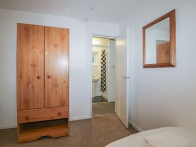 A bedroom with a wooden wardrobe a mirror on the wall and an open door leading to a bathroom at Tamar Cottages 34 in St Ann's Chapel Cornwall
