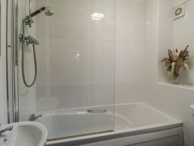 A bathroom with a bathtub shower combination a white sink and a vase with dried plants in a tiled bathroom at Tamar Cottages 34 St Ann's Chapel Cornwall