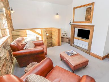 A sitting room with leather armchairs ottoman and a television in a fireplace at Seafield Granary in Alnmouth