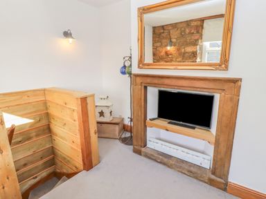 A corner with wooden staircase railing a TV in a wooden fireplace surround and a large mirror above at Seafield Granary in Alnmouth