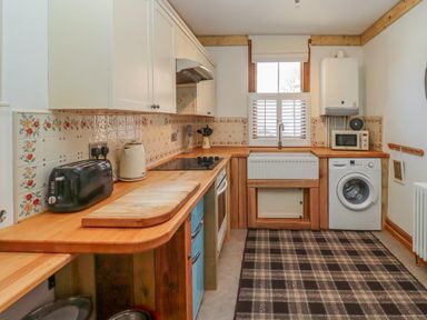 A kitchen with wooden countertops, white cabinets, a toaster, kettle, oven, sink, washing machine and microwave at Seafield Granary in Alnmouth