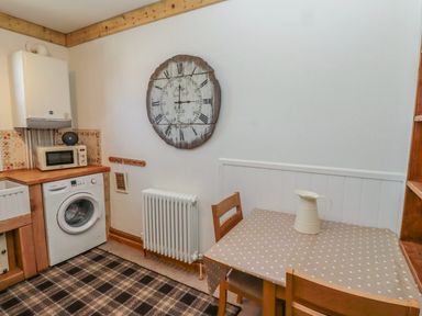 A kitchen corner with a washing machine microwave table with a pitcher chairs and a wall clock at Seafield Granary in Alnmouth