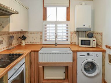 A kitchen with a sink under a window a washing machine and a microwave on a wooden countertop at Seafield Granary in Alnmouth