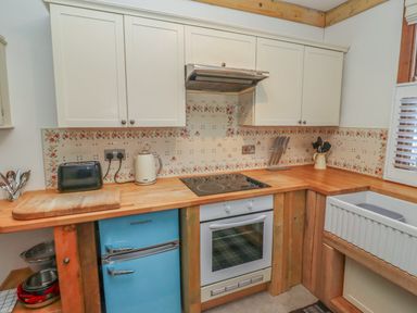 A kitchen with wooden countertops white cabinets a blue Montpellier fridge a white oven and floral patterned tiles at Seafield Granary in Alnmouth
